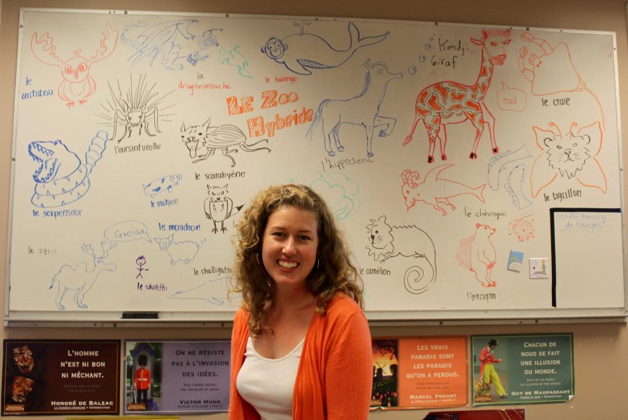 French 2 teacher Melanie Lhomme sits in her classroom in front of a wall of drawings created by students. Photo by ZaZu Lippert.