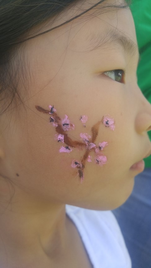 People arrive at the festival and receive a hand-painted cherry blossom branch on their cheek.