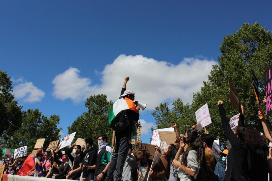 A volunteer with a megaphone speaks and chants on top of the barricade in front of the office.