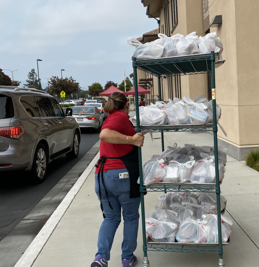 While Fremont High School experiences heavy car traffic, Food Services Assistant Santa Gurrola wheels a cart of packaged meals to the meal pick up location.