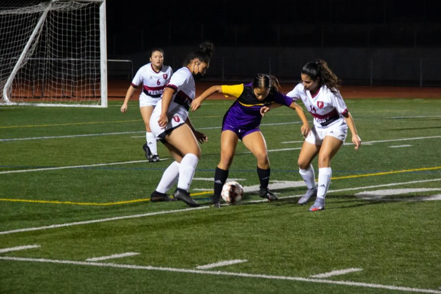 Junior Justine Garcia dribbles the ball, trying to evade two defenders.