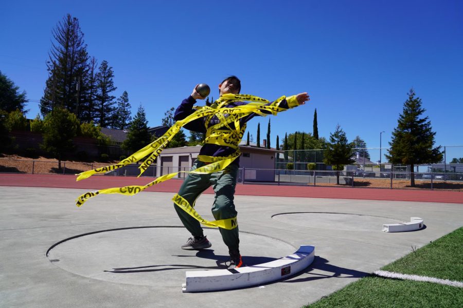 A member of El Estoque throws a shot put while wrapped in caution tape. 