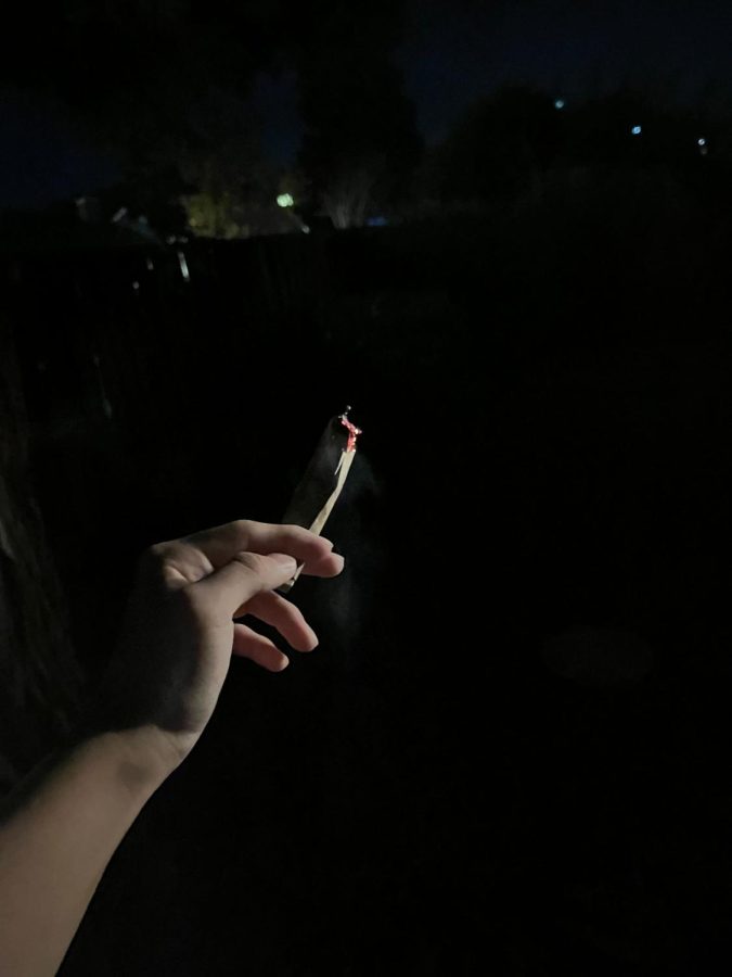 A person holds up a lit cigarette that has been partially smoked.