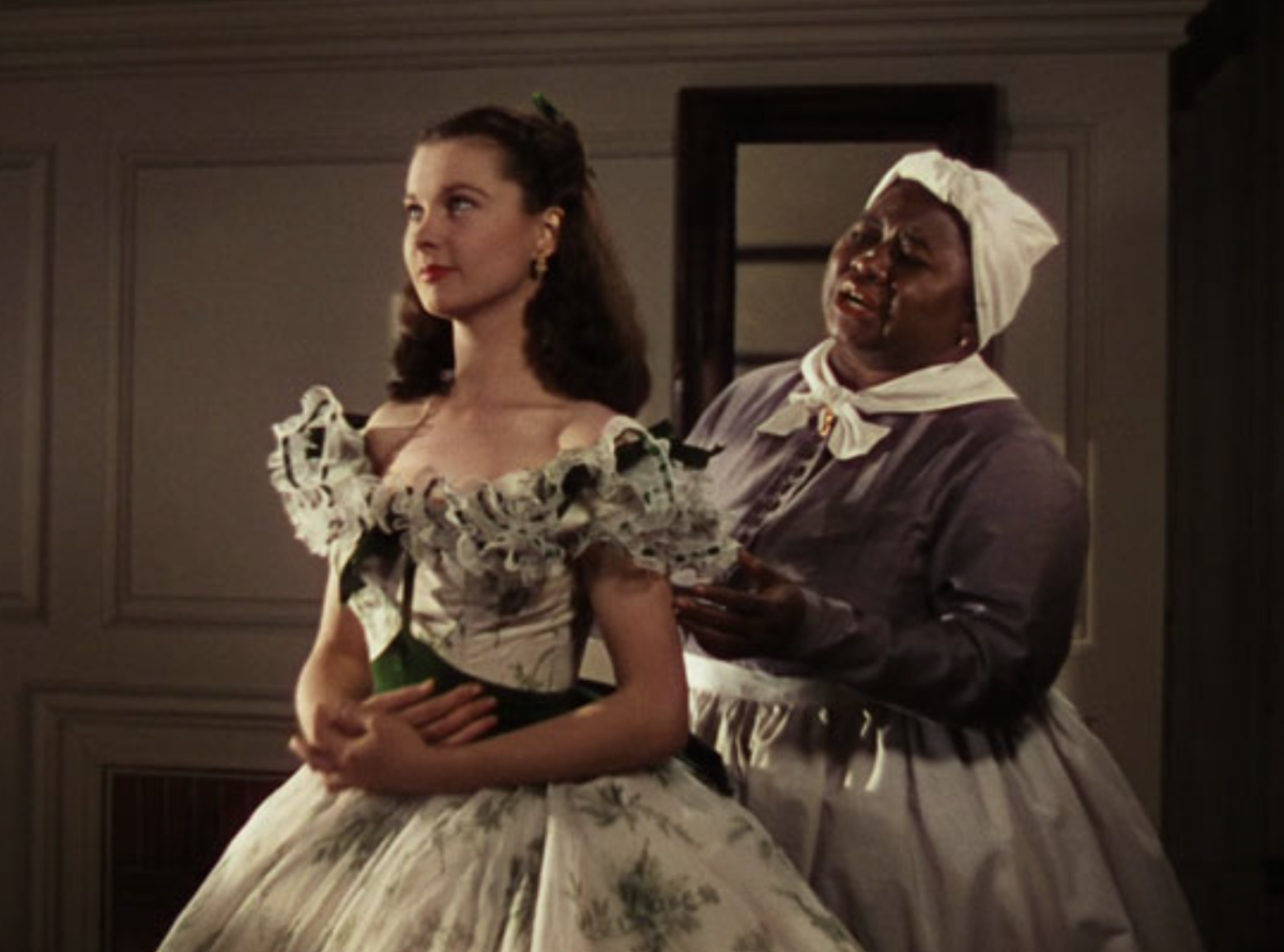 Ruth (Hattie McDaniel) laces up Vivian Leigh (Scarlet O’Hare) while trying to convince her to eat something before leaving. 
