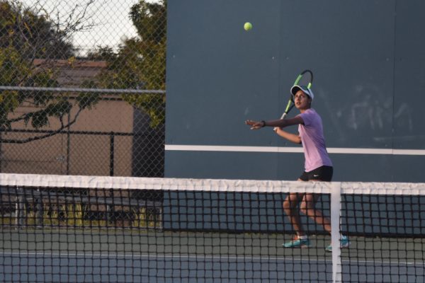 Senior Himani Jha swings backward with her left hand guiding her as she does a forehand stroke. 

