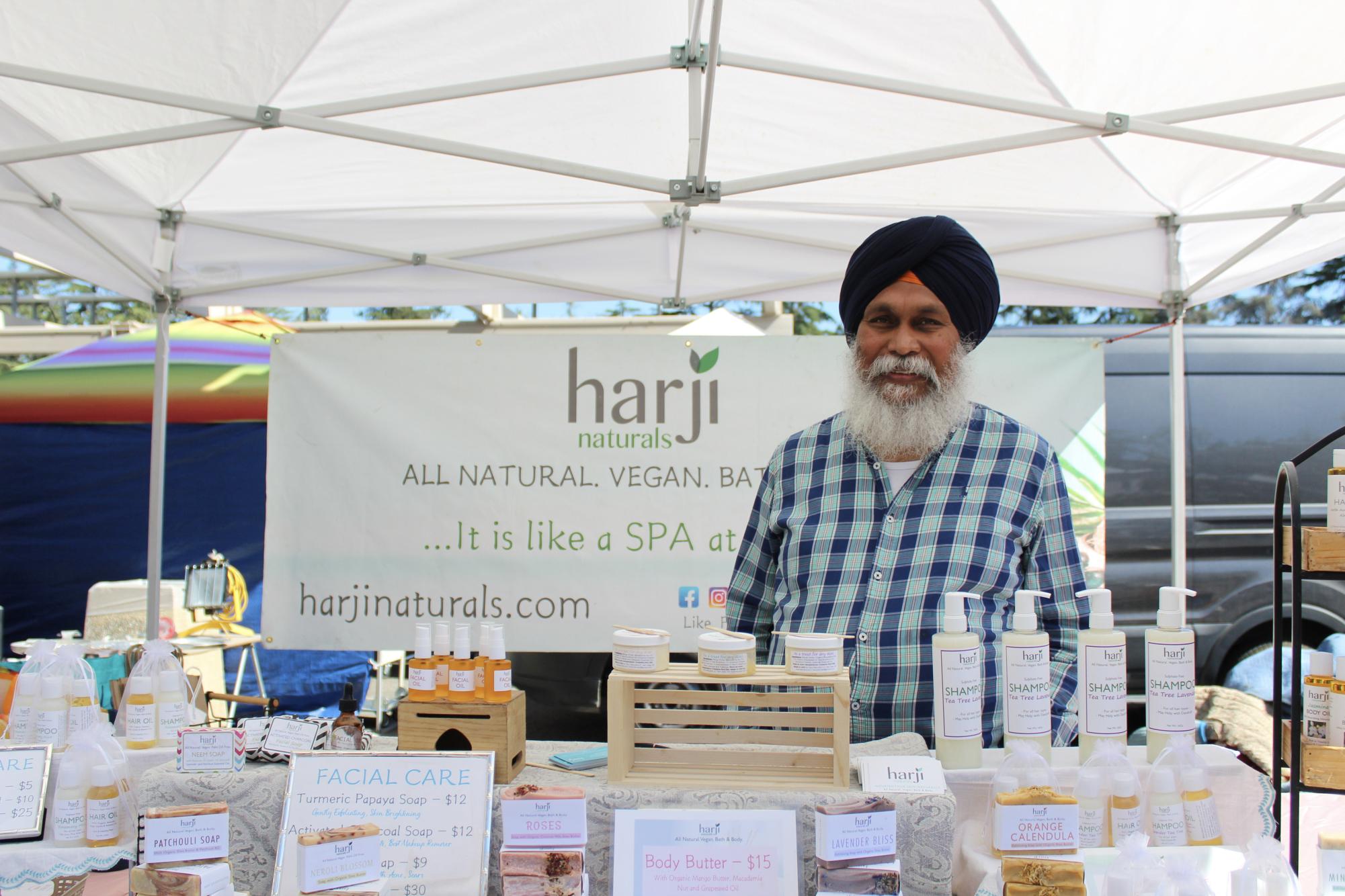 Gurinder Singh poses in front of his products, a display of deodorants, creams, shampoos, and oils. 