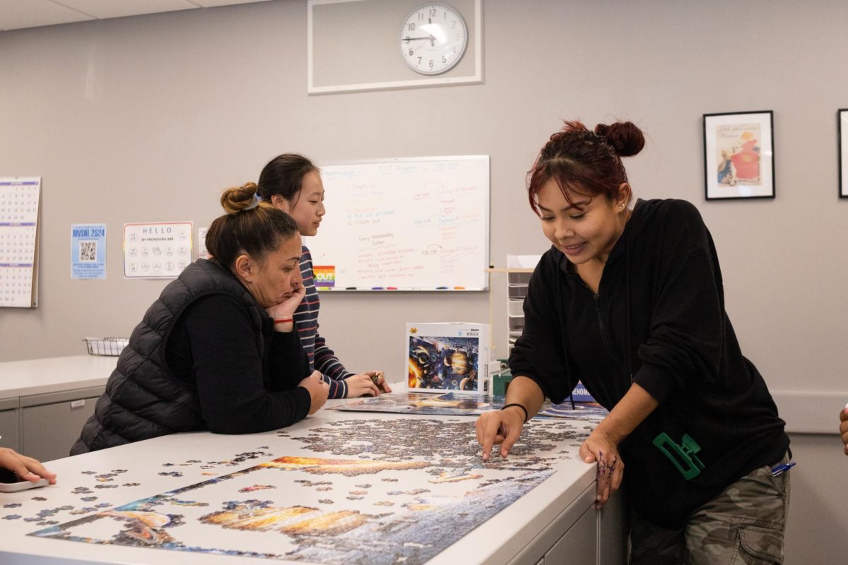 Print technician Paula Gaspar works on a puzzle with students at the print center. 