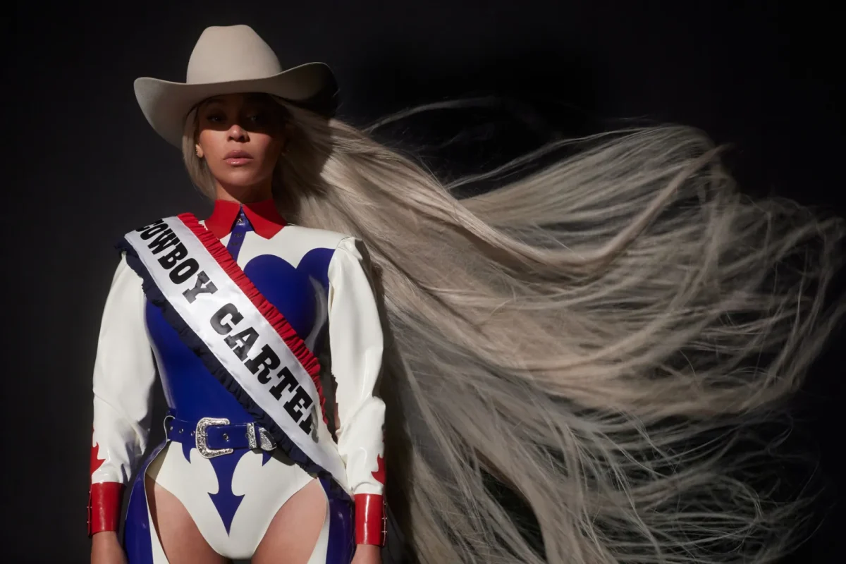 Carter rides a white horse on the main COWBOY CARTER album cover, a parallel with her RENAISSANCE album which features her on a mirror disco ball horse. In her hands is an American flag, and she is decked out in a red, white and blue cowboy outfit.