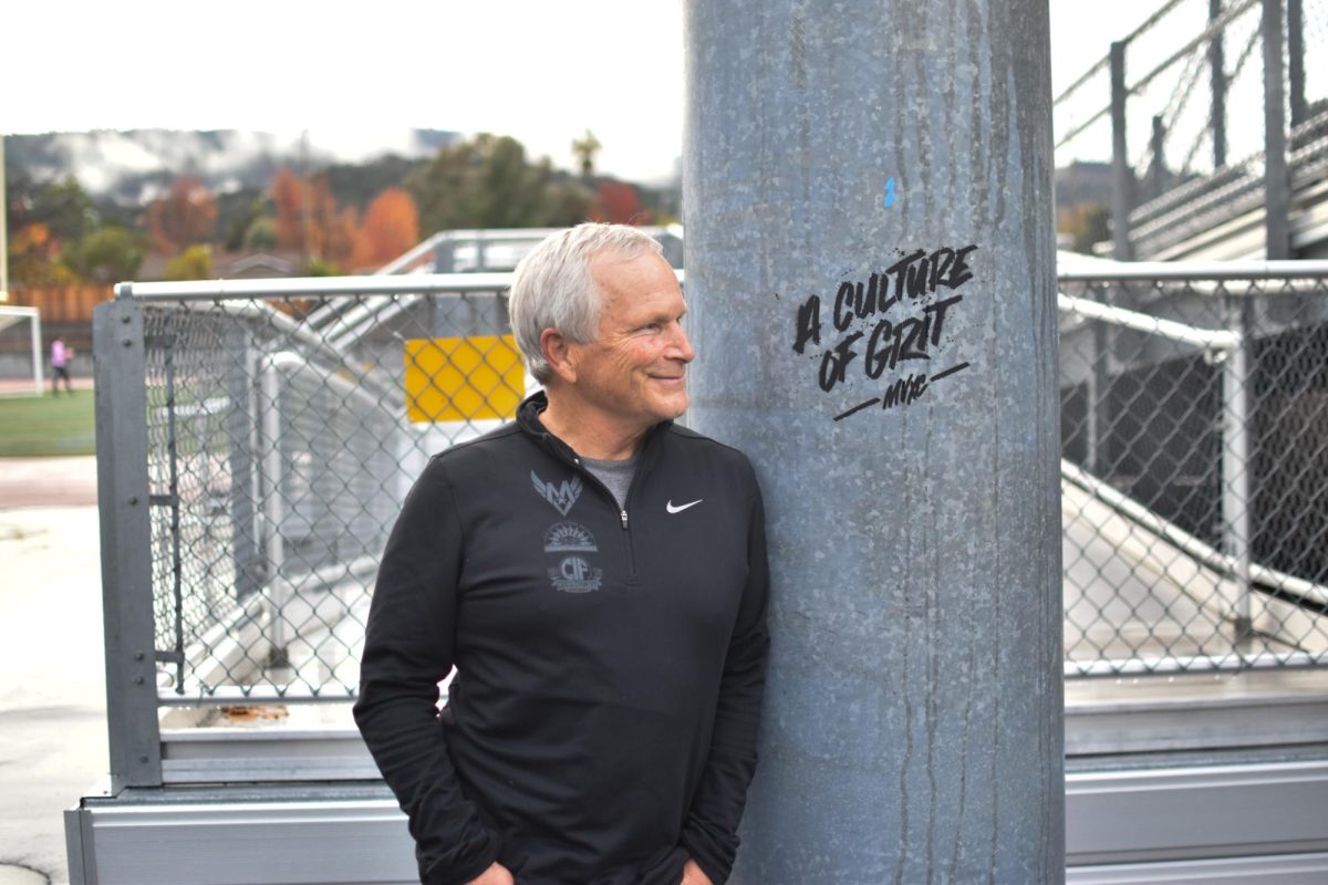 Cross Country coach Kirk Flatow poses next to the pole that runners tap after their runs. Photo | Ethan Kellogg