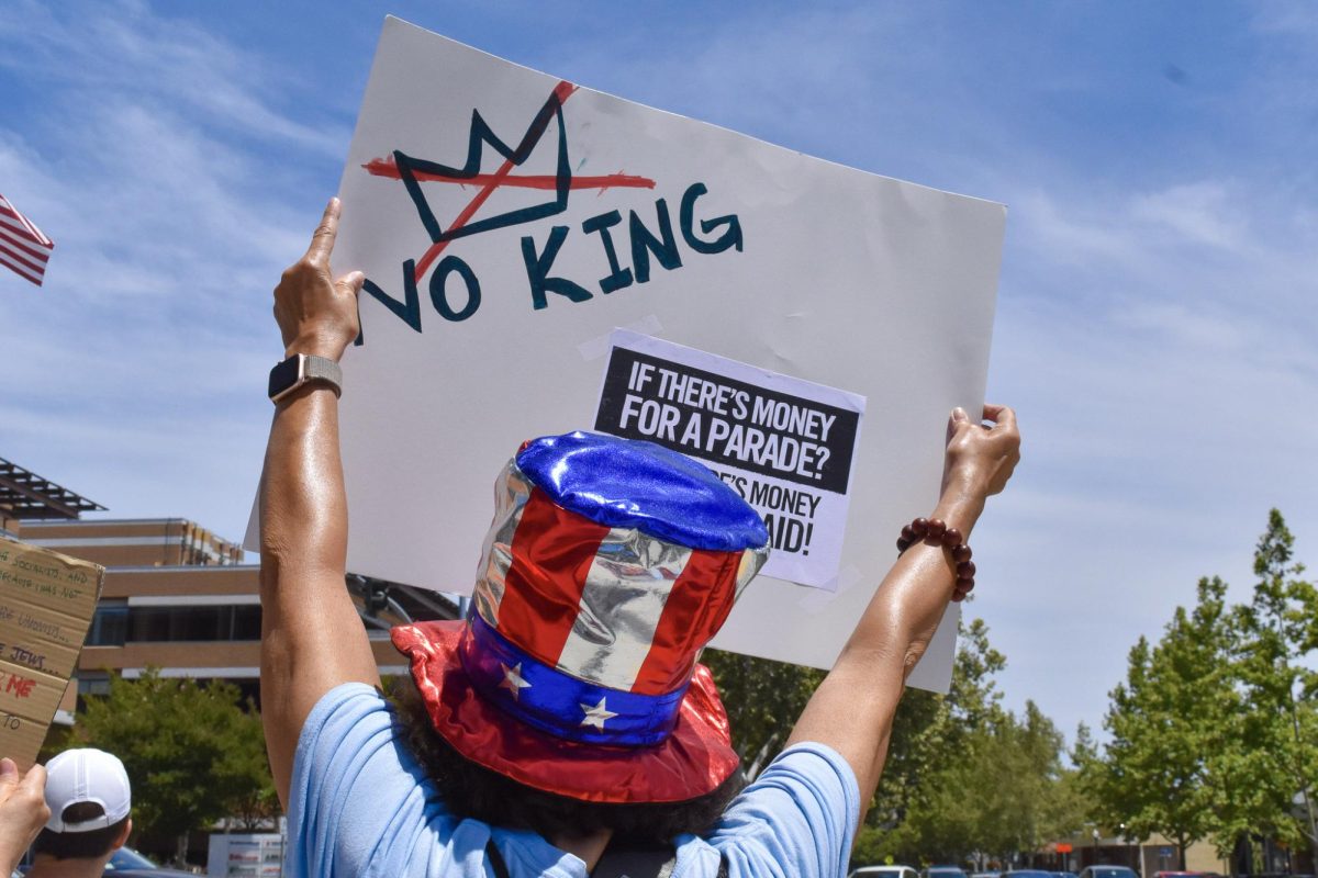 An attendee holds a “NO KING” poster facing the intersection of Castro Street and El Camino Real.