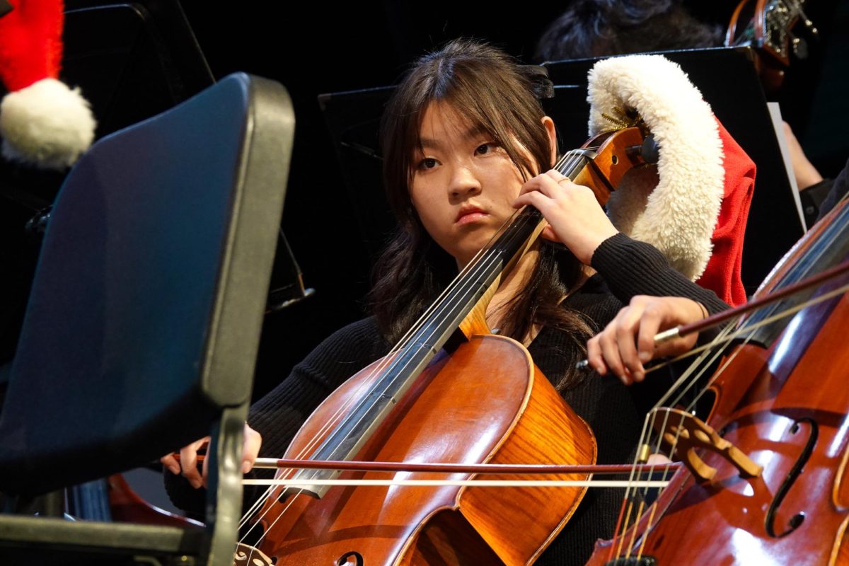 Sophomore and cellist Abigail Ran focuses intently on her sheet music, performing "Sleigh Ride" by Leroy Anderson festively with a Santa hat on her cello. Photo | Grace Lin