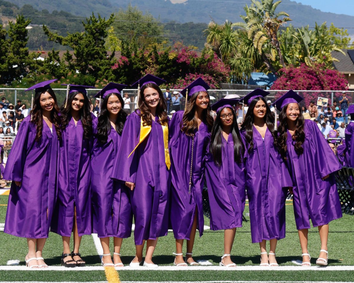 Decked in purple, seniors Courtney Masli, Trisha Mahajan, Emily Lin, Nicole Jeleva, Leah Desai, Anvika Verma, Alaina Agarwal and Miya Sakurai (left to right) smile towards the crowd as their parents take pictures of them. Photo | Emmy Harimoto